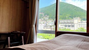 Quarto de hotel com uma cama, uma mesa e vista para uma área montanhosa com edifícios.