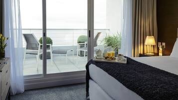 A hotel room with a bed, a tray with breakfast items, a nightstand with a lamp, and a view of the balcony with outdoor furniture.