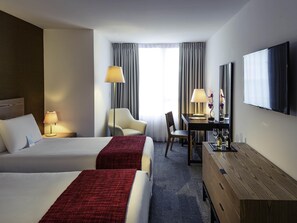 A hotel room with two beds, a desk with a lamp, a chair, a TV, and a window with curtains. - Mercure Montevideo Punta Carretas (Montevideo)