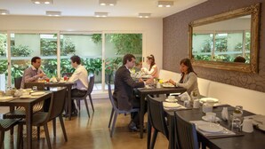 A dining area with tables set for four people each, large windows with a view of greenery, and a mirror on the wall. - Mercure Montevideo Punta Carretas (Montevideo)