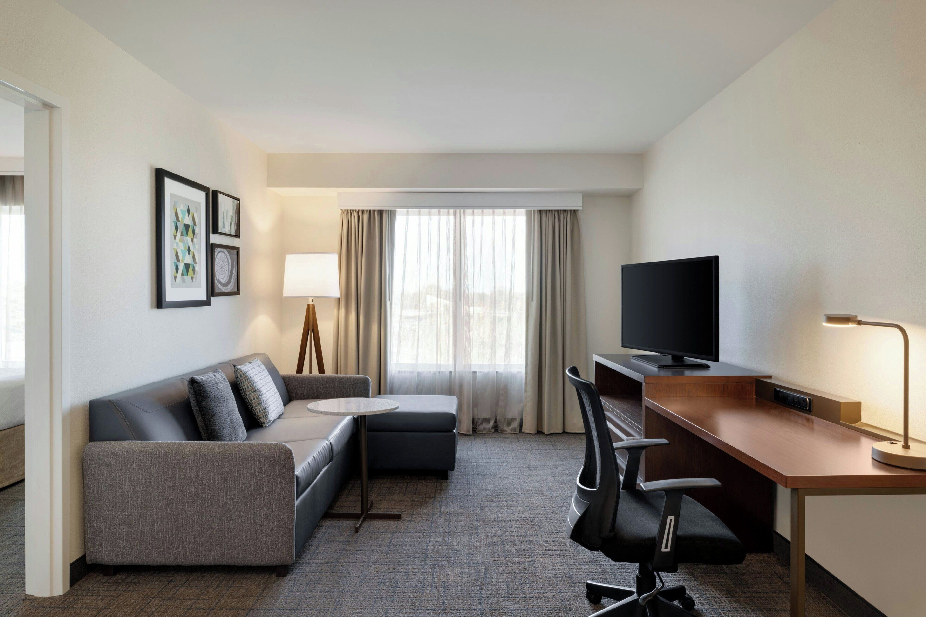 Ein Hotelzimmer mit Sofa, Schreibtisch, Stuhl, Fernseher und Lampe.