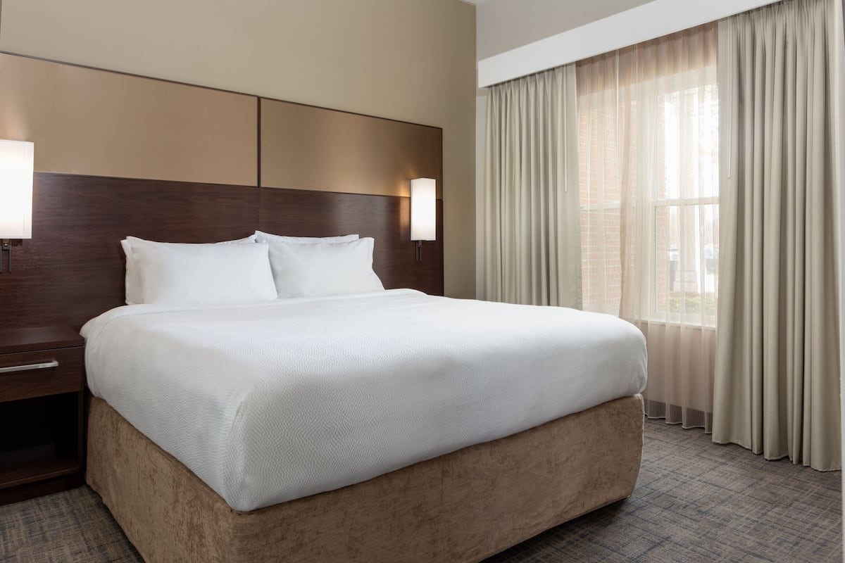 A hotel room with a large bed, a nightstand, a lamp, and a window with curtains.