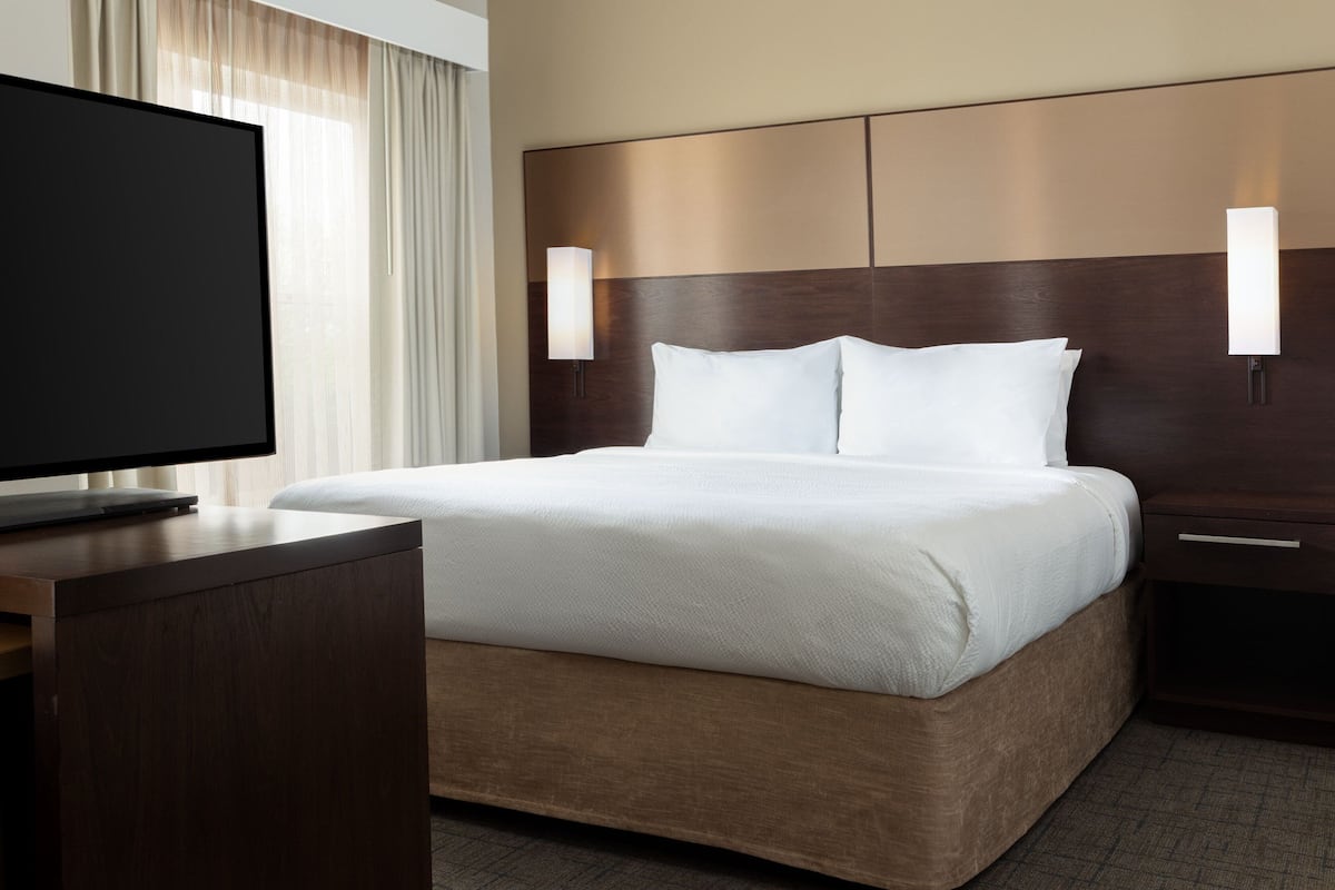A hotel room with a large bed, a flat-screen TV, and two wall-mounted lamps.