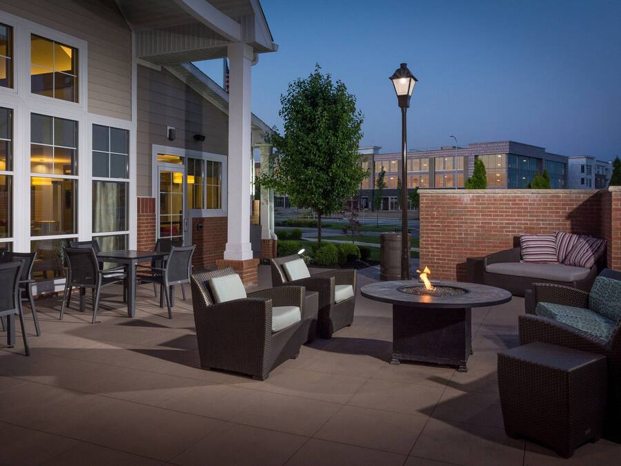 An outdoor patio area with wicker furniture, a fire pit, and a view of a building with large windows and a brick wall.