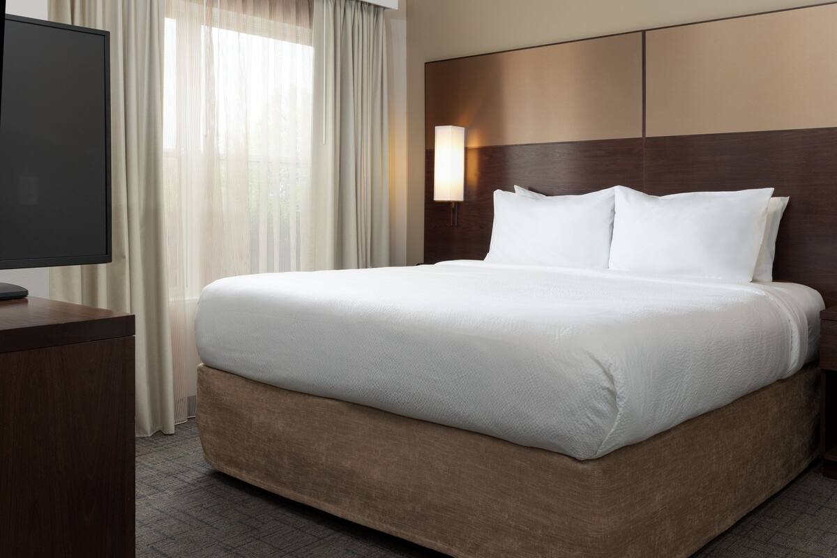 A hotel room with a large bed, a TV on a wooden desk, and a window with curtains.