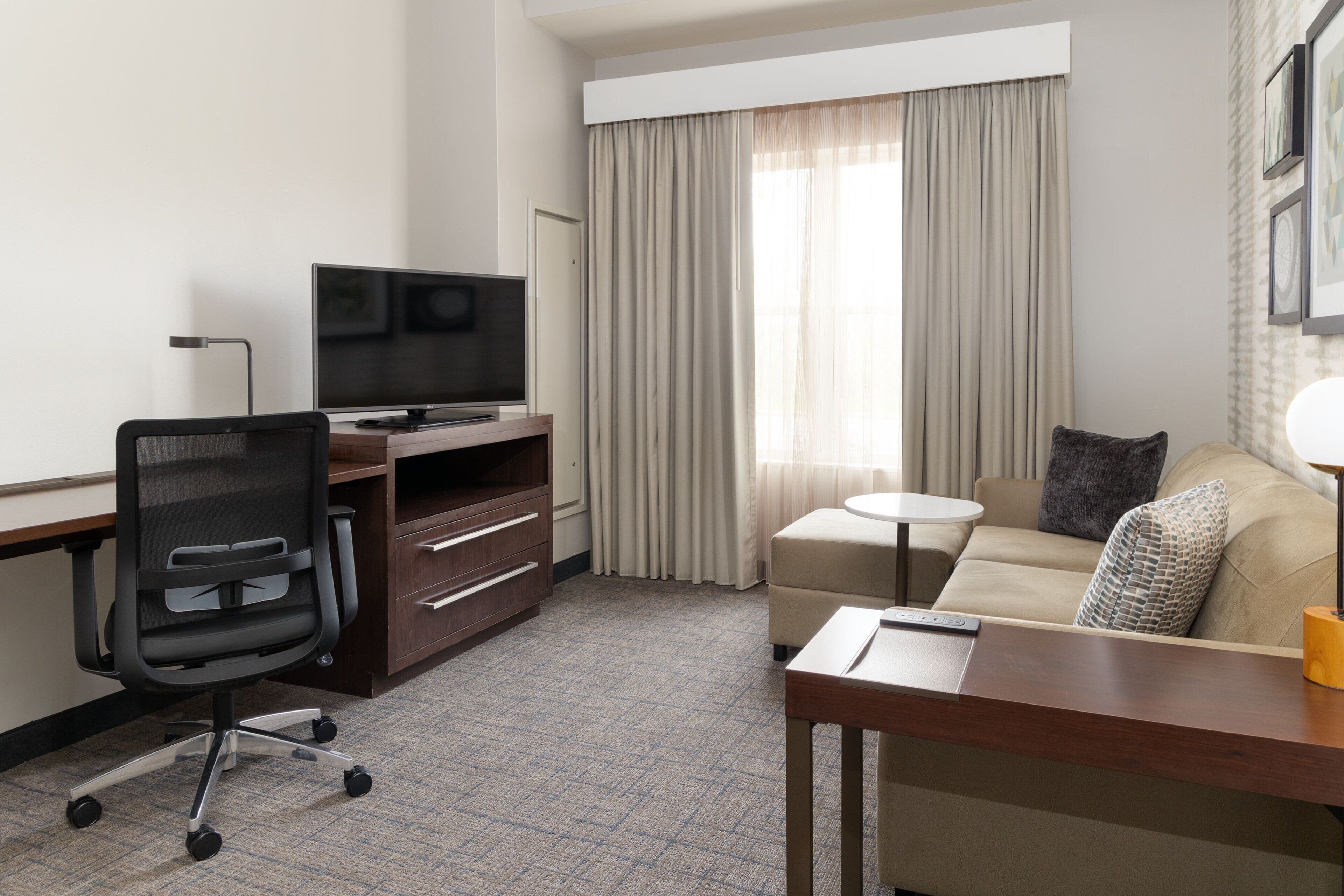 Habitación de hotel con escritorio, silla, televisor, sofá y cortinas.