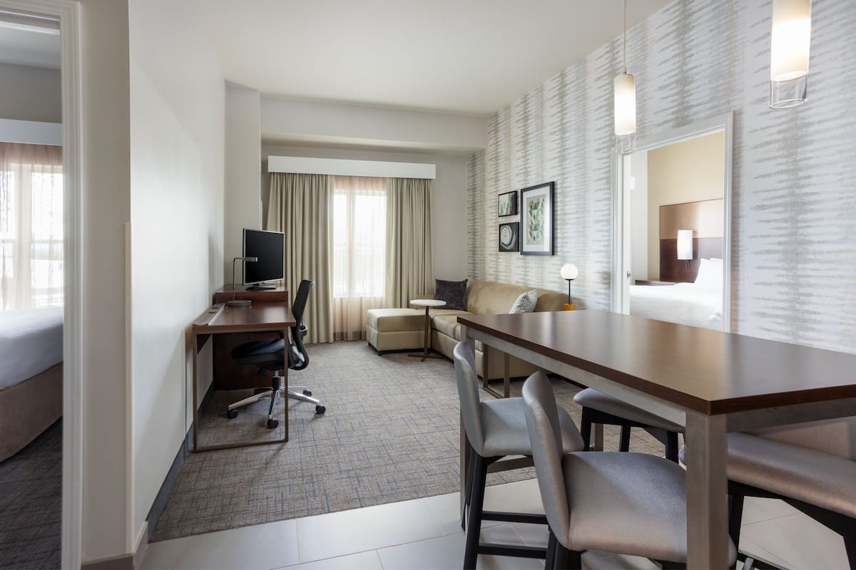 A hotel room with a desk, office chair, sofa, and a small round table.