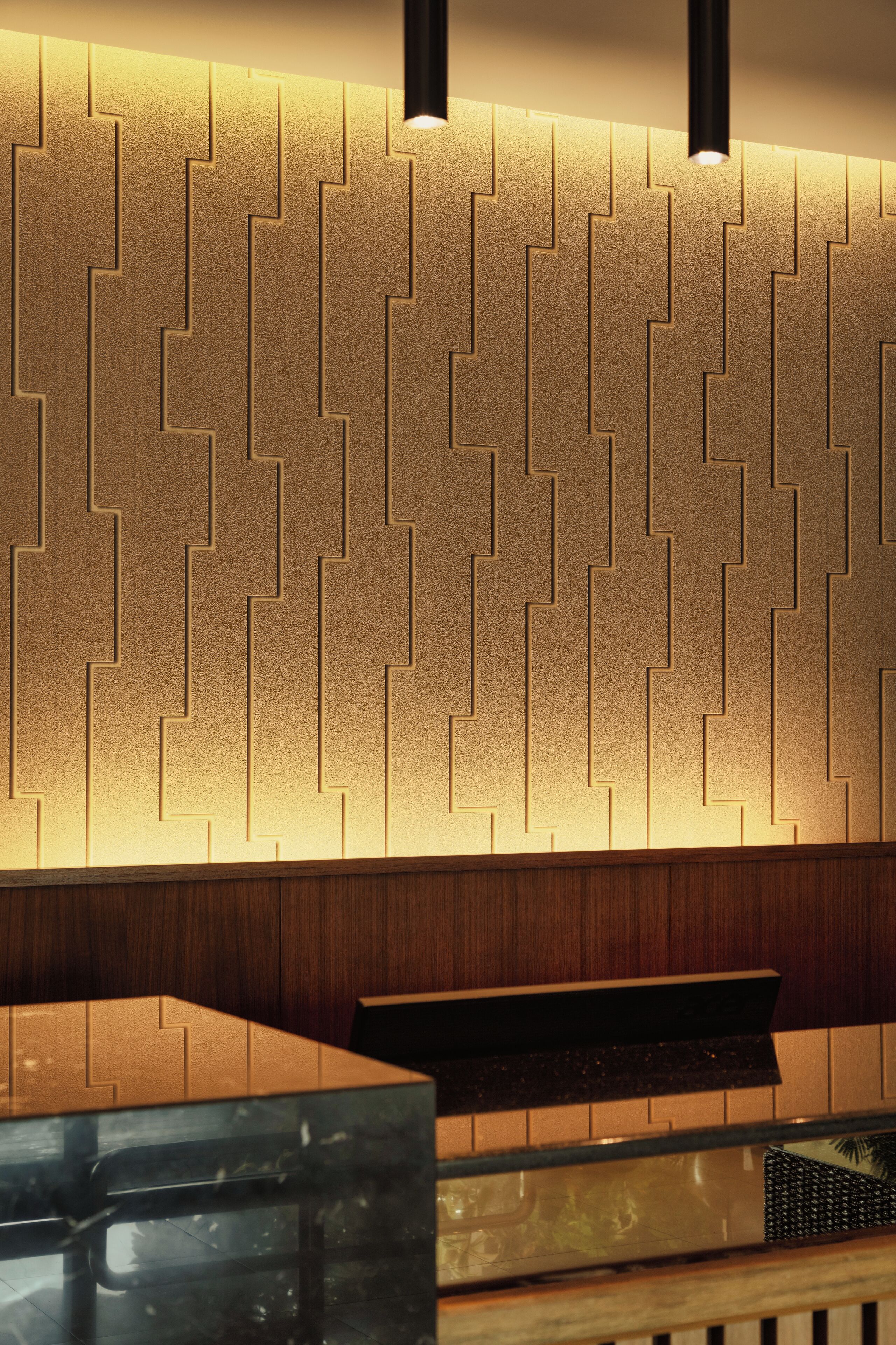 Un interior moderno con una pared de diseño geométrico, una encimera de madera y una lámpara colgante negra.