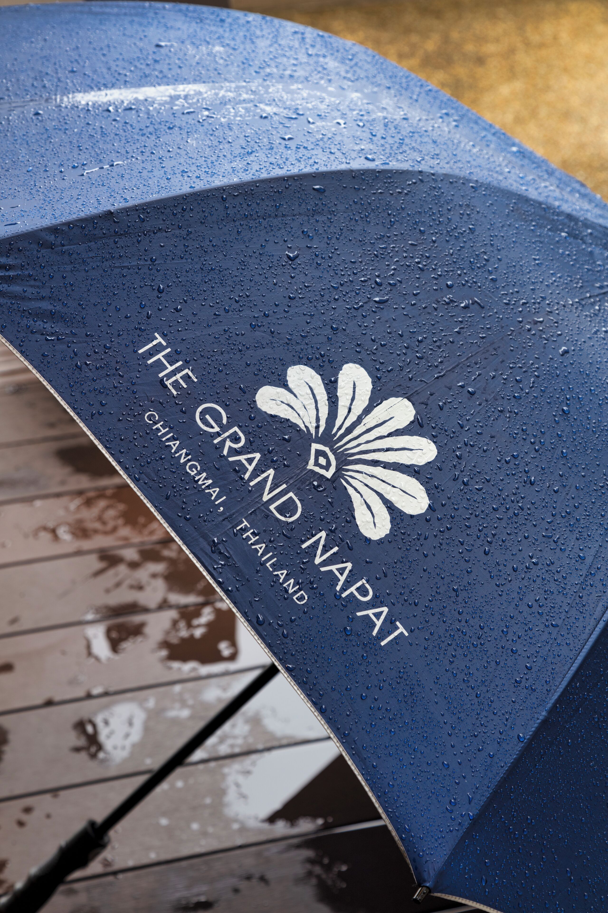 A blue umbrella with the text "THE GRAND NAPAT Chiang Mai, Thailand" and a white flower logo.