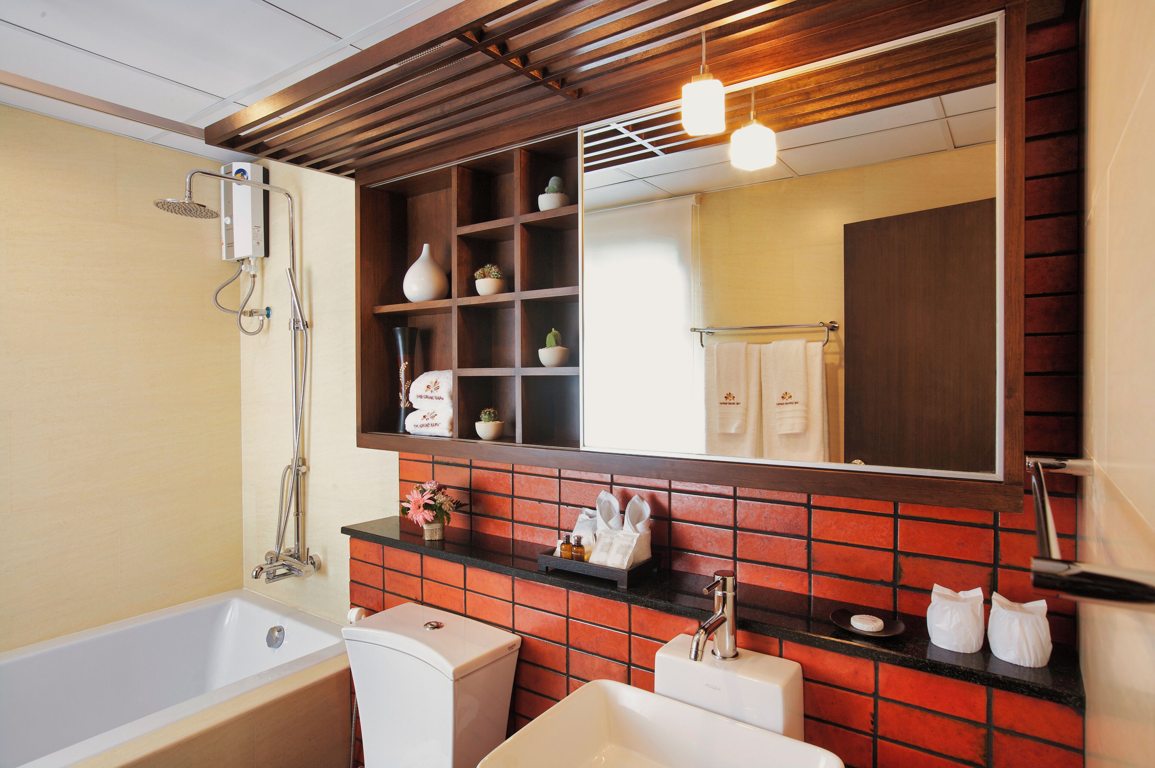 Un baño moderno con bañera, lavamanos y ducha. Cuenta con un espejo grande, un estante con objetos decorativos y un salpicadero de azulejos rojos.