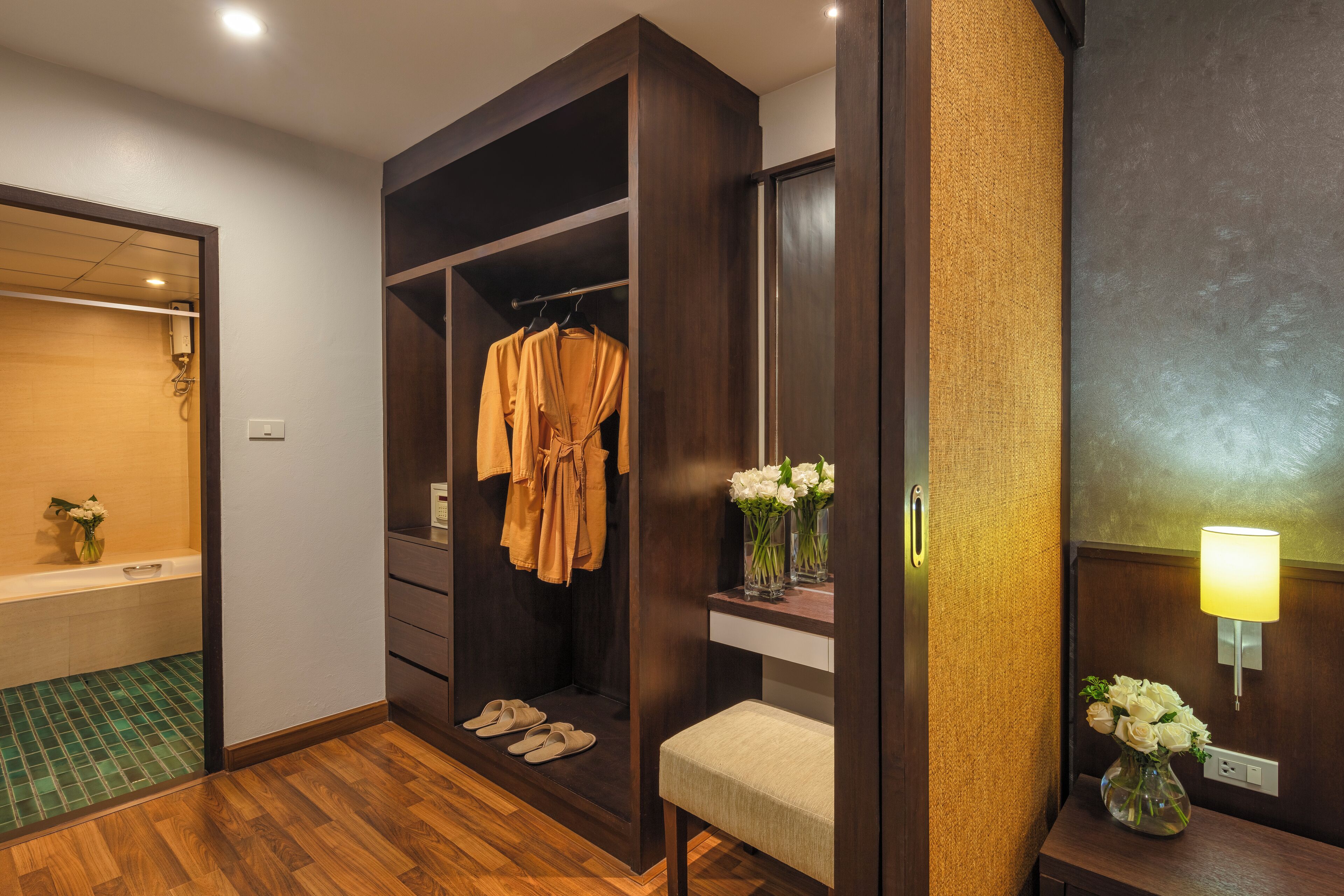 A walk-in closet with a robe hanging, a bench, and a vase with flowers.