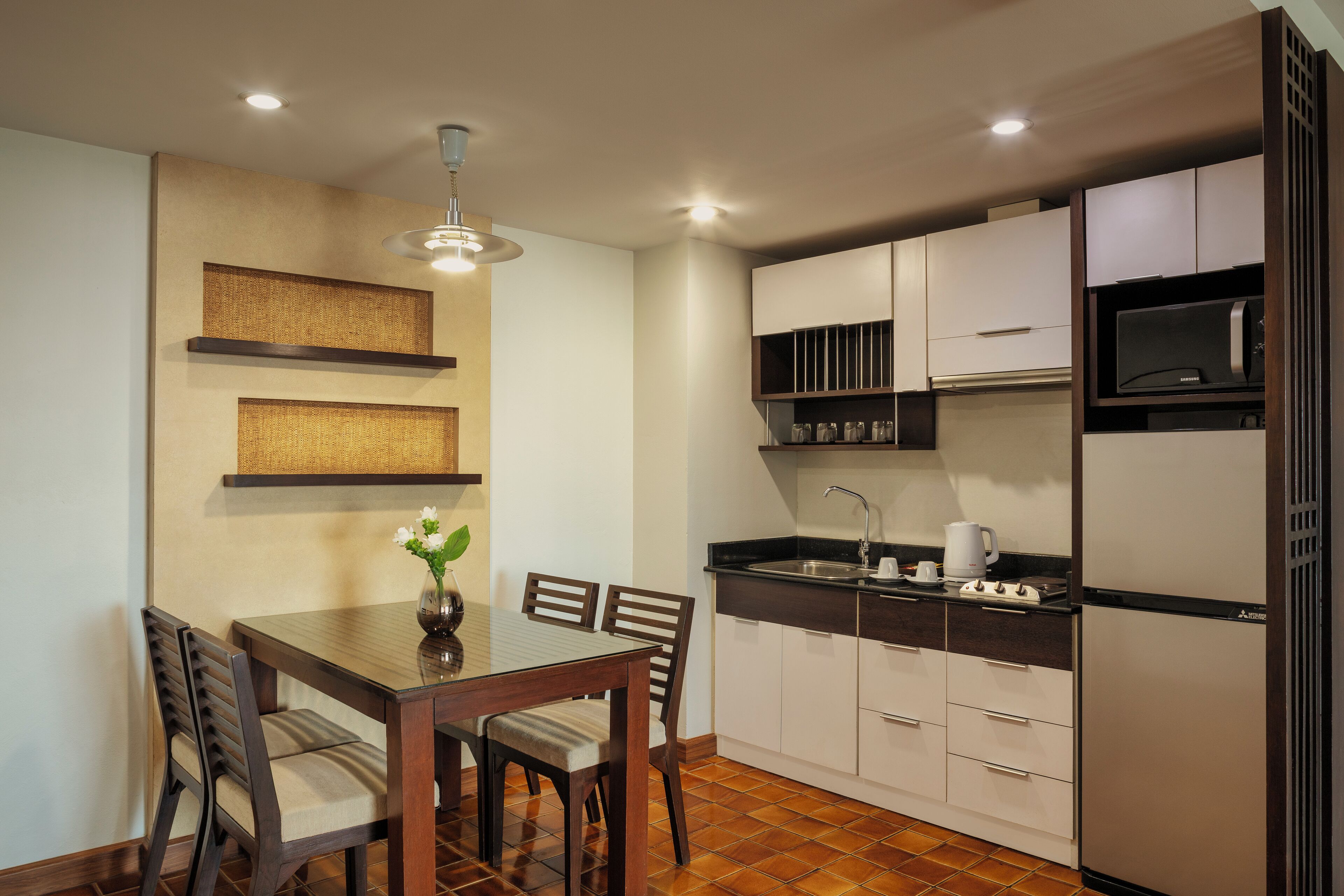 A compact kitchen with a dining area, featuring a wooden table, chairs, a hanging light fixture, and built-in cabinets.