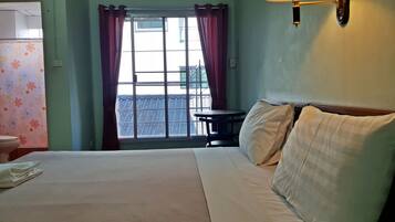 Una habitación de hotel con cama, una mesa, una lámpara, vista al exterior y un inodoro.