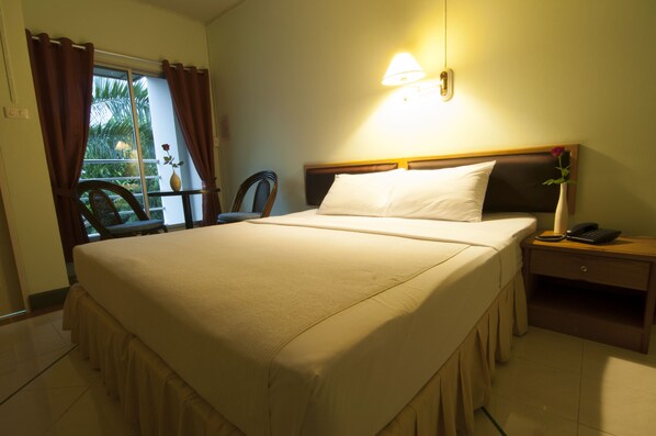 Quarto de hotel com uma cama grande, mesa de cabeceira com telefone, uma cadeira e janela com cortinas.