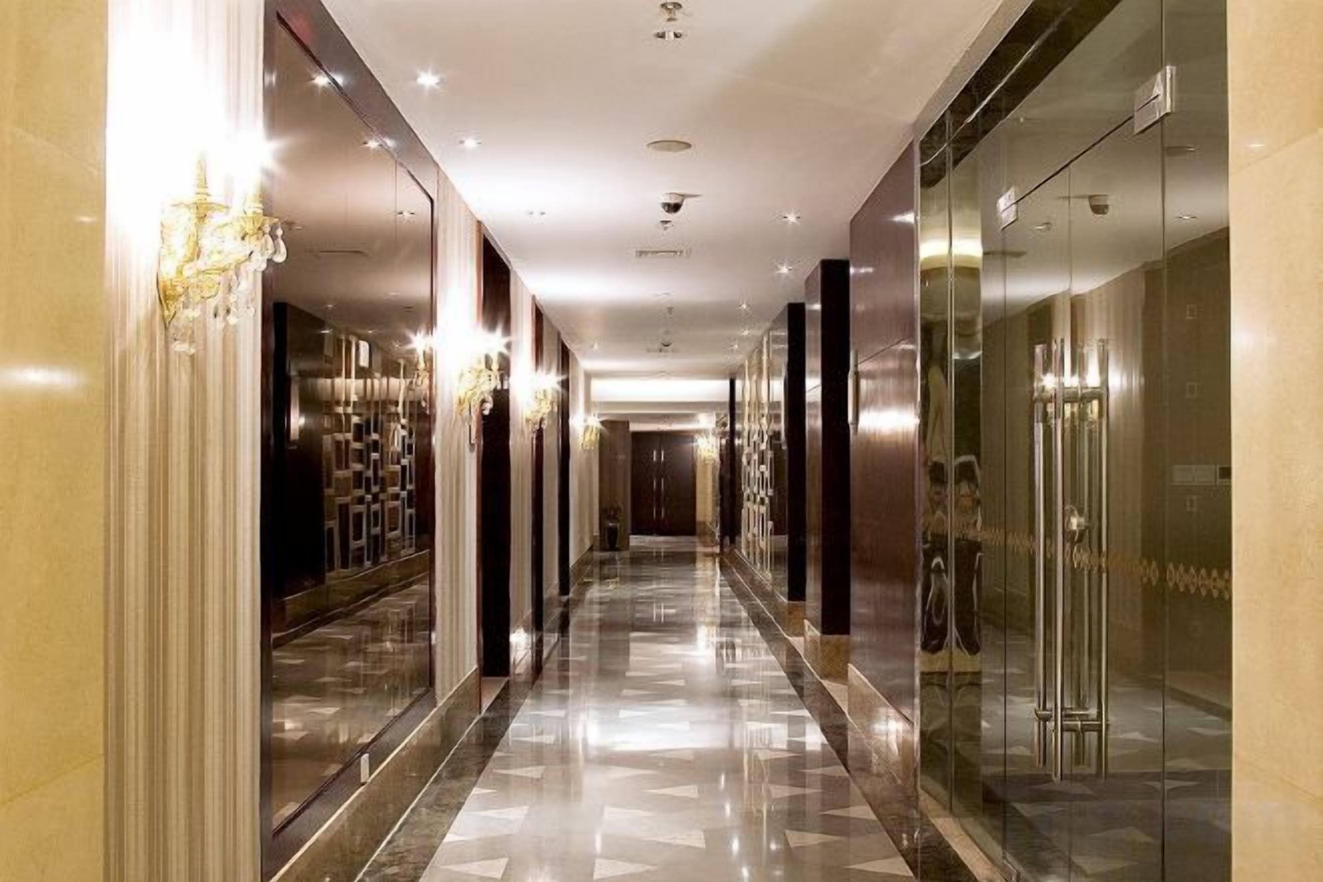 A long, narrow hallway with reflective floors and glass doors on both sides, leading to a door at the end.