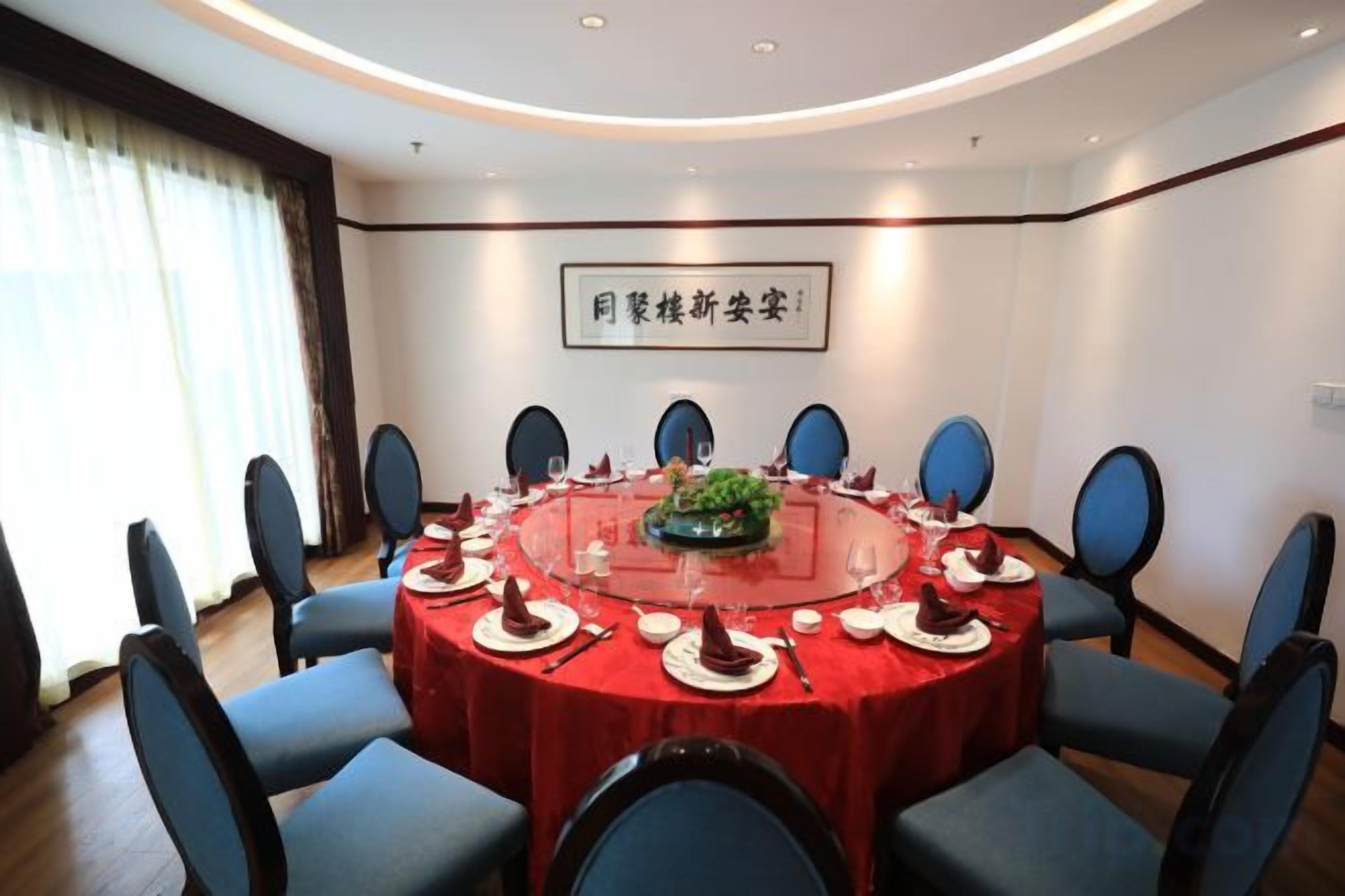 Une salle de conférence avec une table ronde, des chaises bleues et une nappe rouge.