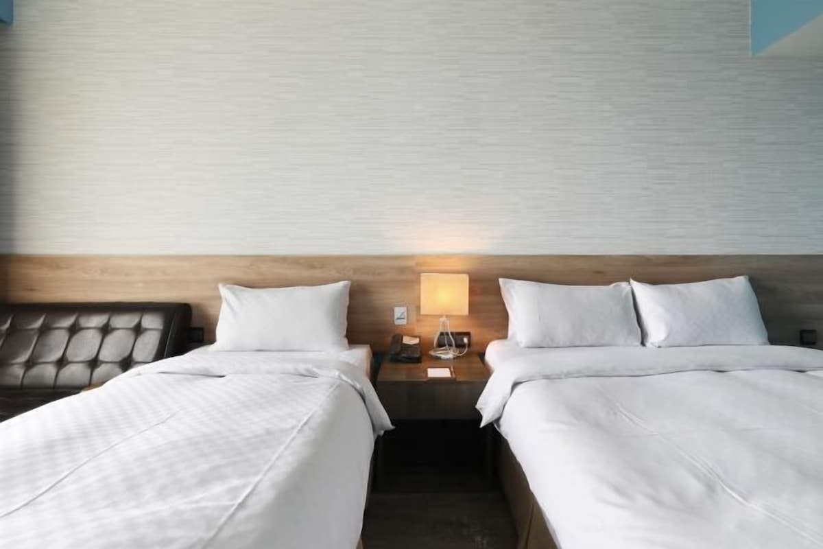 A hotel room with two beds, a wooden headboard, a nightstand with a lamp, and a wall with a textured pattern.