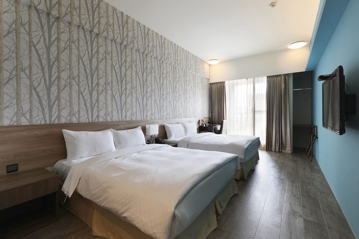 A hotel room with two beds, a wooden headboard, a large mirror, a flat-screen TV, and a window with curtains.