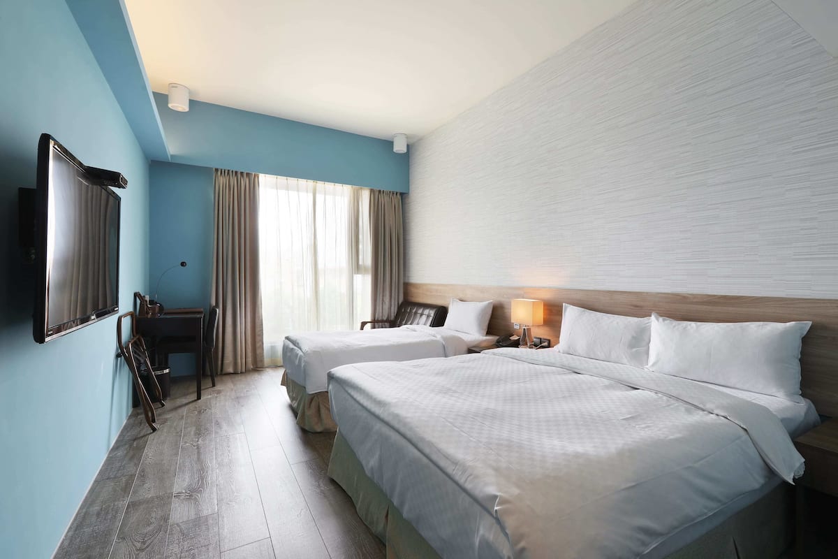 A hotel room with two beds, a desk, a chair, and a TV.