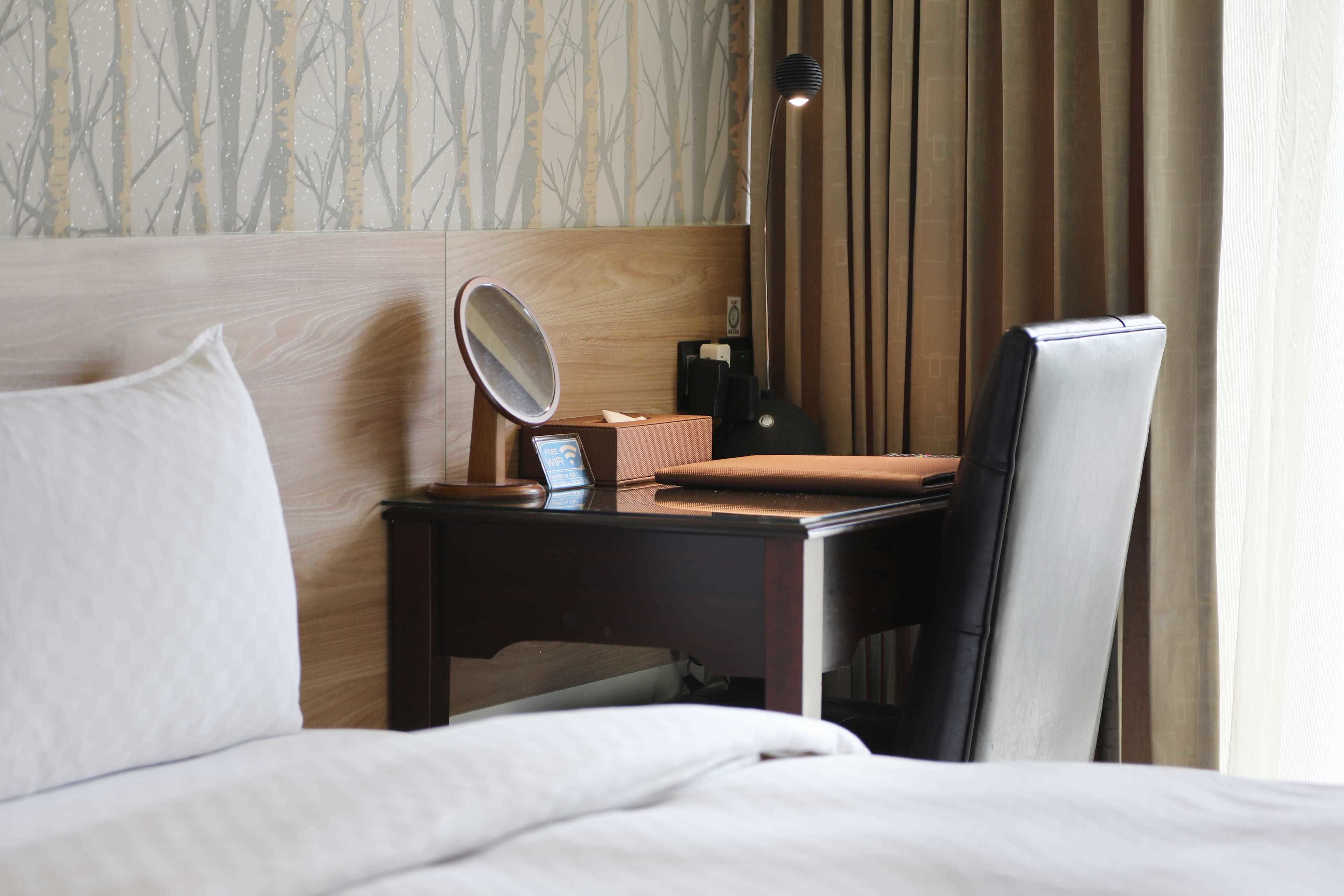 Habitación de hotel con cabecera de madera, mesita de noche con lámpara, una silla y cama con ropa blanca.