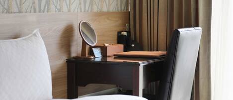 Habitación de hotel con cabecera de madera, mesita de noche con lámpara, una silla y cama con ropa blanca.