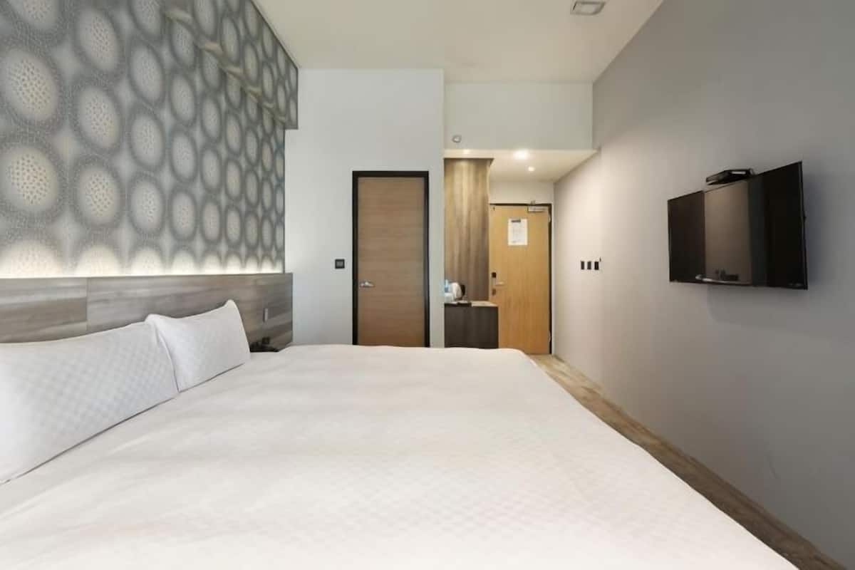 A hotel room with a large bed, a TV mounted on the wall, and a patterned wall design.