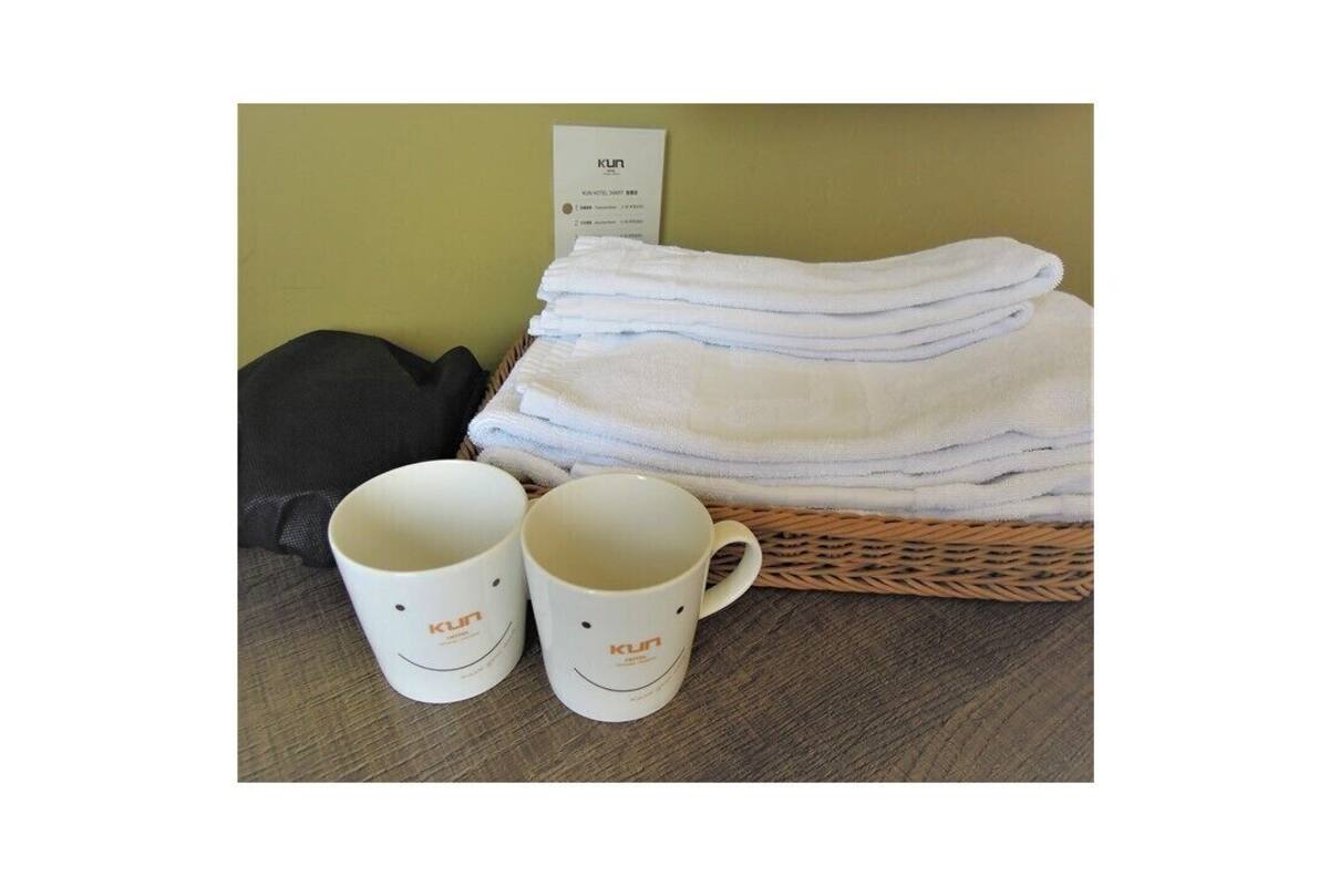 A stack of white towels and two white mugs with a logo on a wooden table against a green wall.