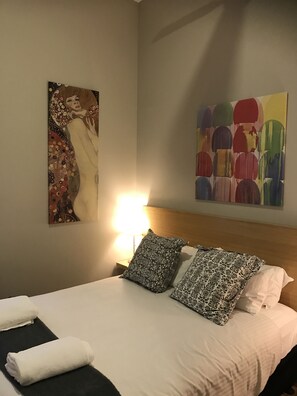 Une chambre d’hôtel avec un lit, des oreillers, une table de chevet, une lampe et deux œuvres d’art accrochées au mur.