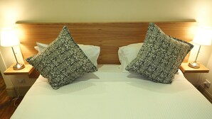Una cama con dos almohadones estampados, un cabecero de madera y lámparas de noche.