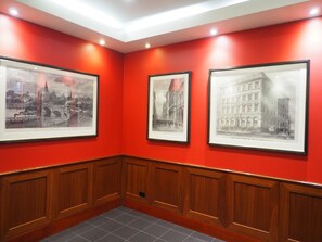 A hallway with red walls, wooden paneling, and three framed black and white cityscape photographs.