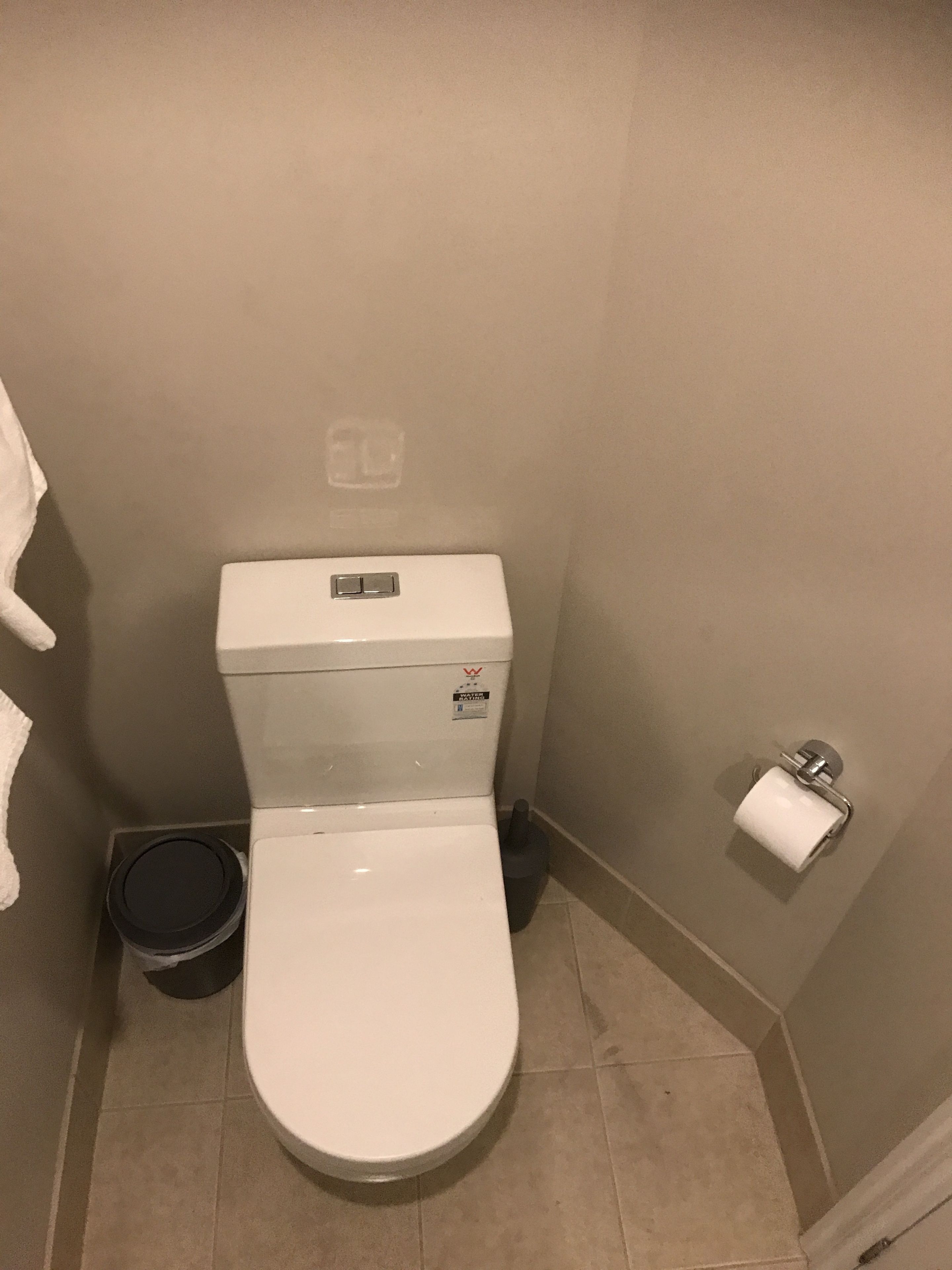 A small, compact bathroom with a white toilet, a trash can, and a toilet paper holder on the wall.