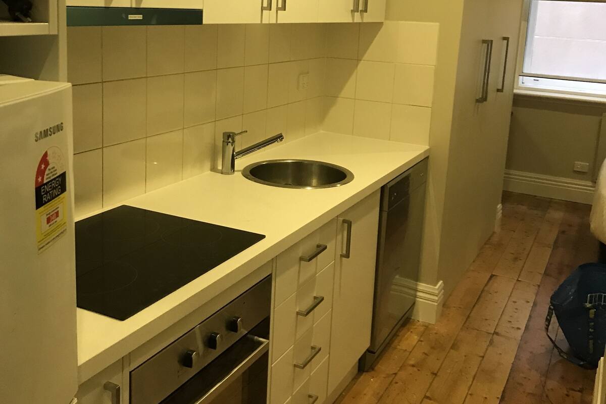 Una cocina compacta con armarios blancos, un lavamanos de acero inoxidable y un horno empotrado.