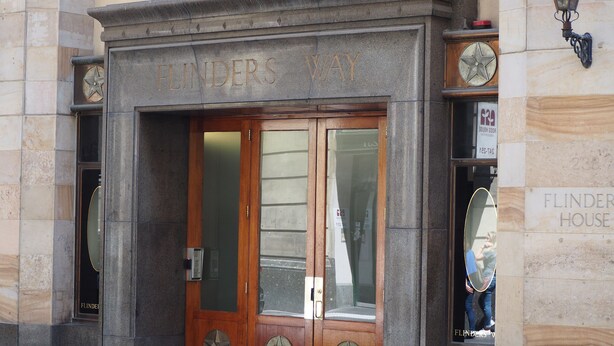Entrada de un edificio con un cartel que dice 'FLINDERS WAY' y una puerta con diseño en forma de estrella.