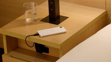 A wooden bedside table with a white electronic device and a glass of water.