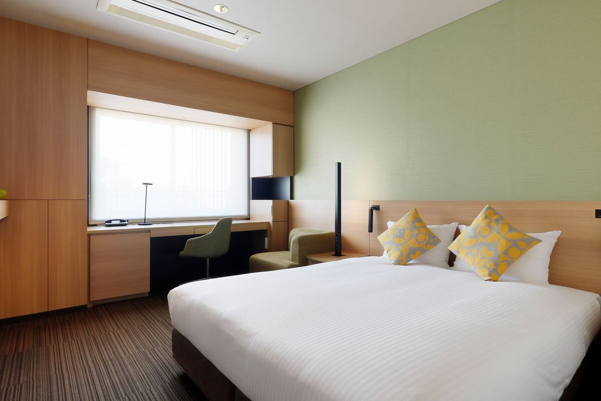 A hotel room with a large bed, a desk, a chair, and a window.