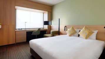 A hotel room with a large bed, a desk, a chair, and a window.