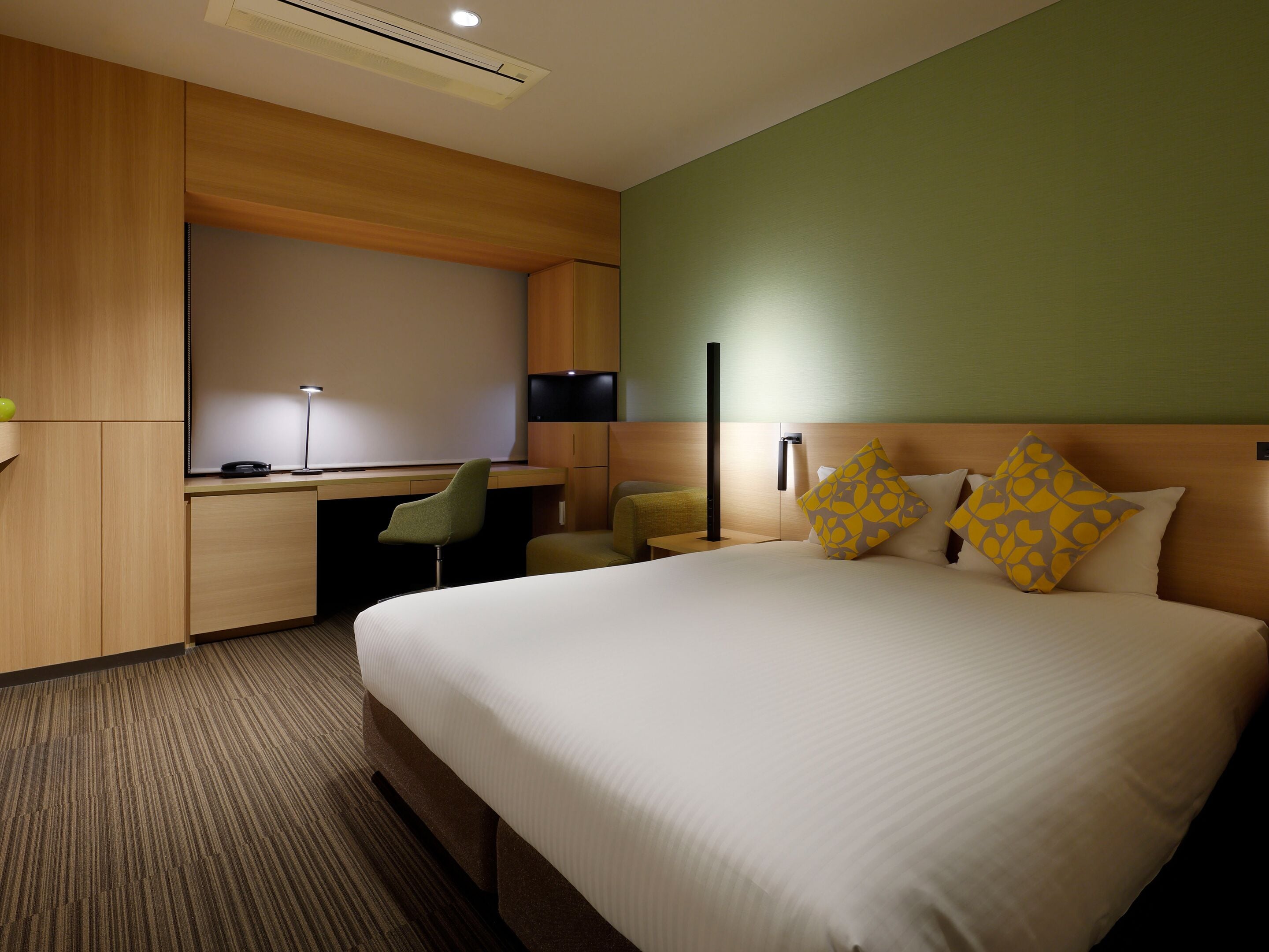 A hotel room with a bed, a desk, a chair, a television, and a wall-mounted light.