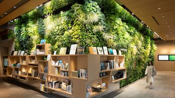 A modern hotel lobby with a large vertical garden wall, a well-lit reading area with bookshelves, and a clean, contemporary design.