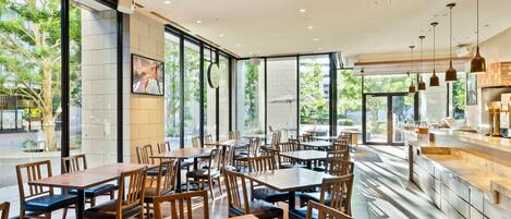 Un restaurante espacioso con amplias ventanas, mesas y sillas de madera, y un diseño de interiores moderno.
