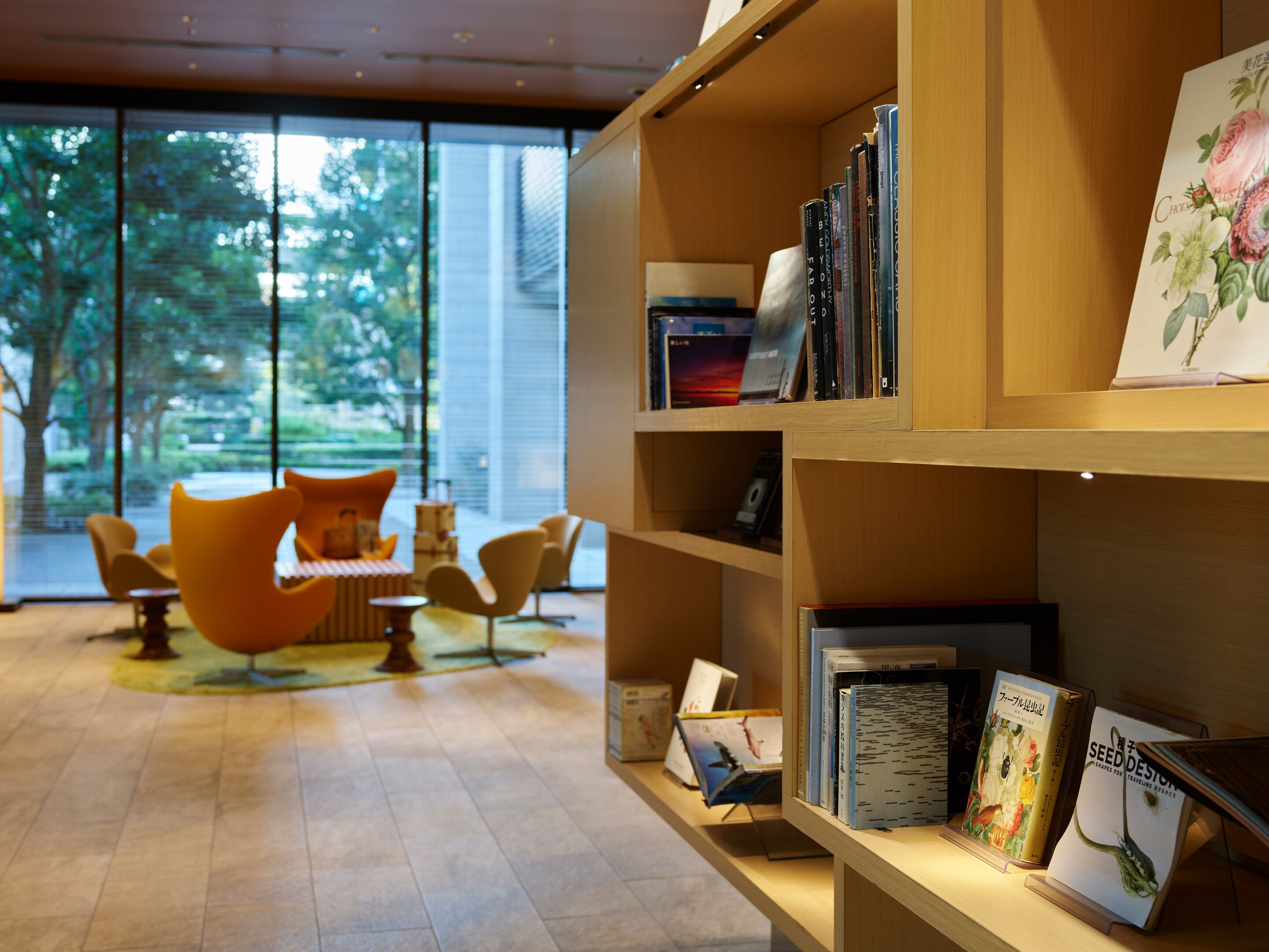 Een modern interieur met een houten boekenkast, een zithoek met oranje stoelen, en uitzicht door grote ramen.