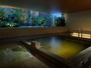 A tranquil indoor pool area with a stone border, a wooden ceiling, and a view of lush greenery outside. - Mitsui Garden Hotel Kashiwanoha Chiba (Kashiwa)