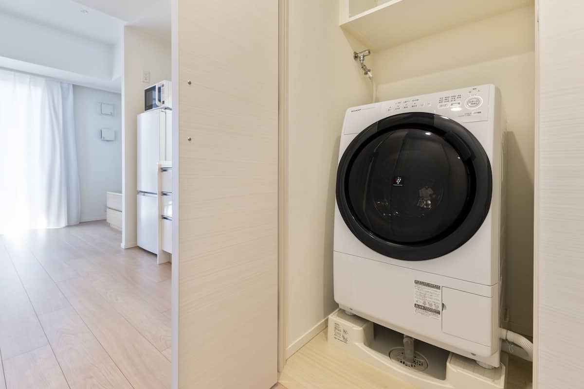 A compact, modern laundry room with a front-loading washing machine, a small cabinet, and a microwave.