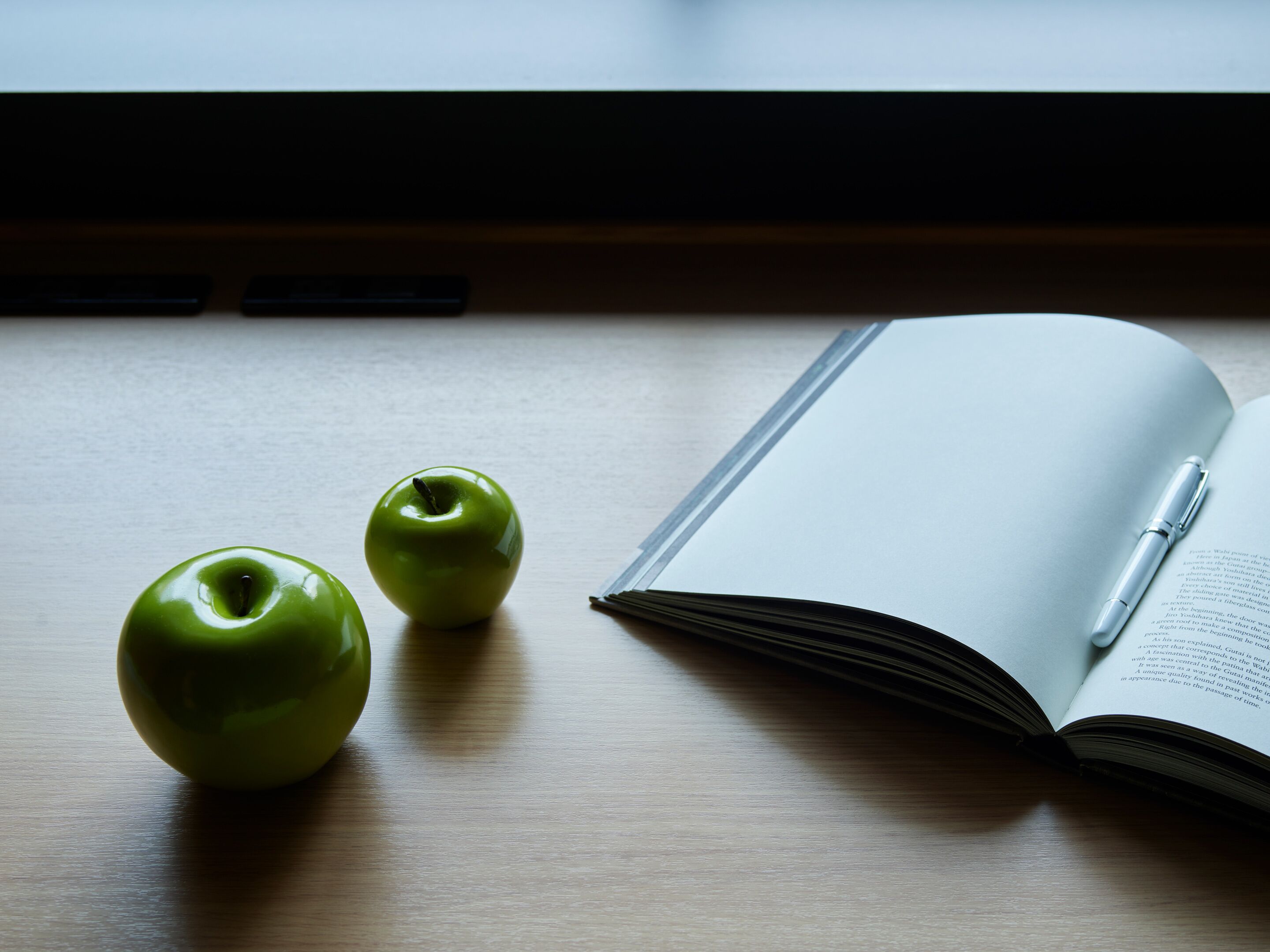 Ein Holztisch mit zwei Äpfeln und einem offenen Buch, auf dem ein Stift liegt.