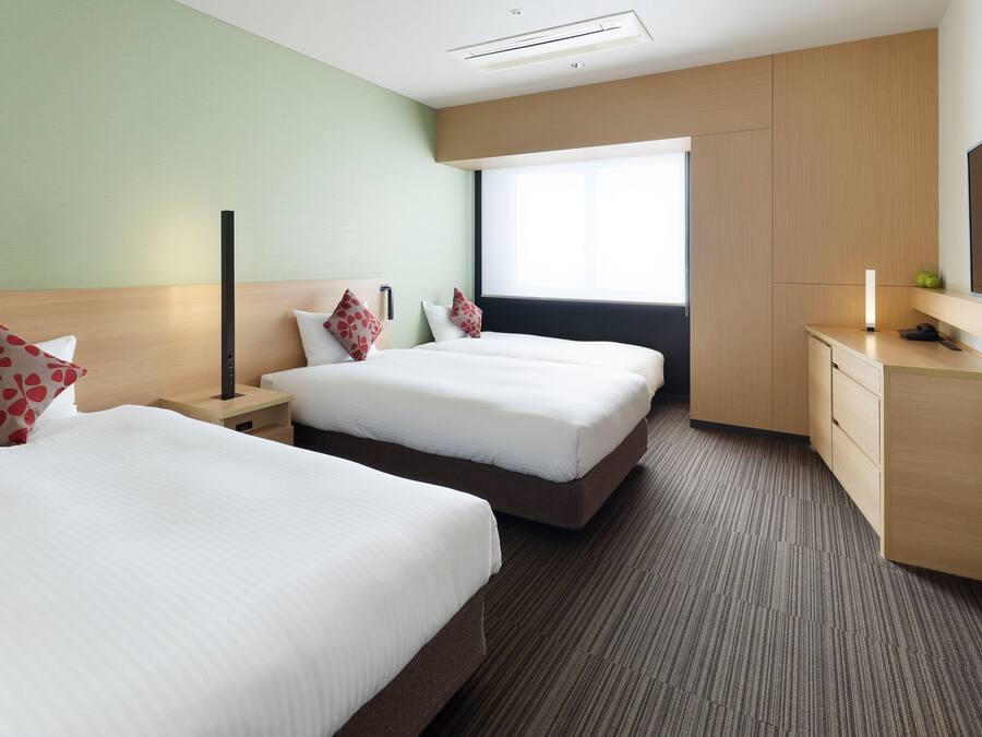 A hotel room with two beds, a nightstand, a desk, a mirror, and a window with blinds.