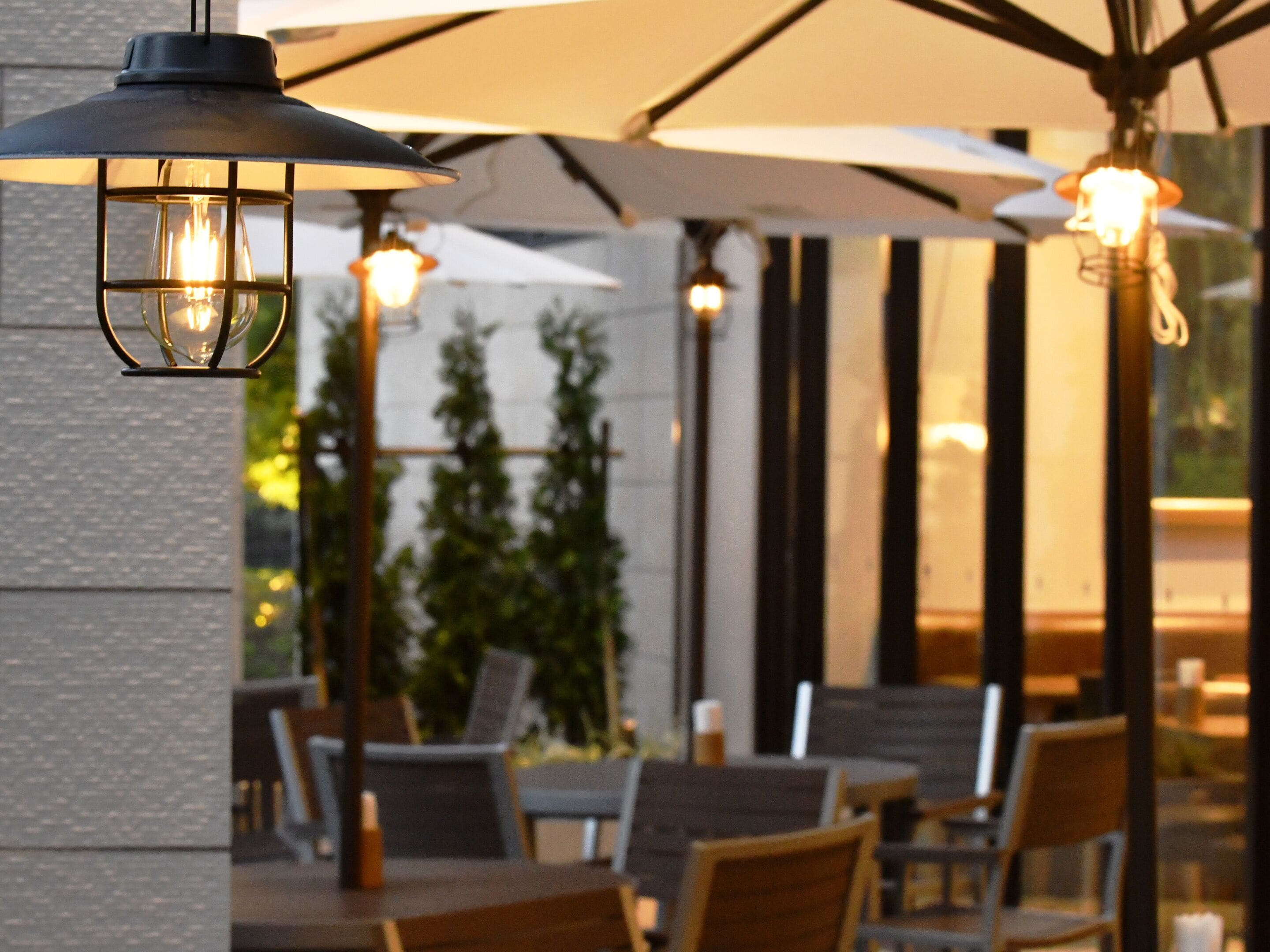 Un espace extérieur aménagé avec des tables et des chaises, des parasols et des lampes suspendues de style lanterne.