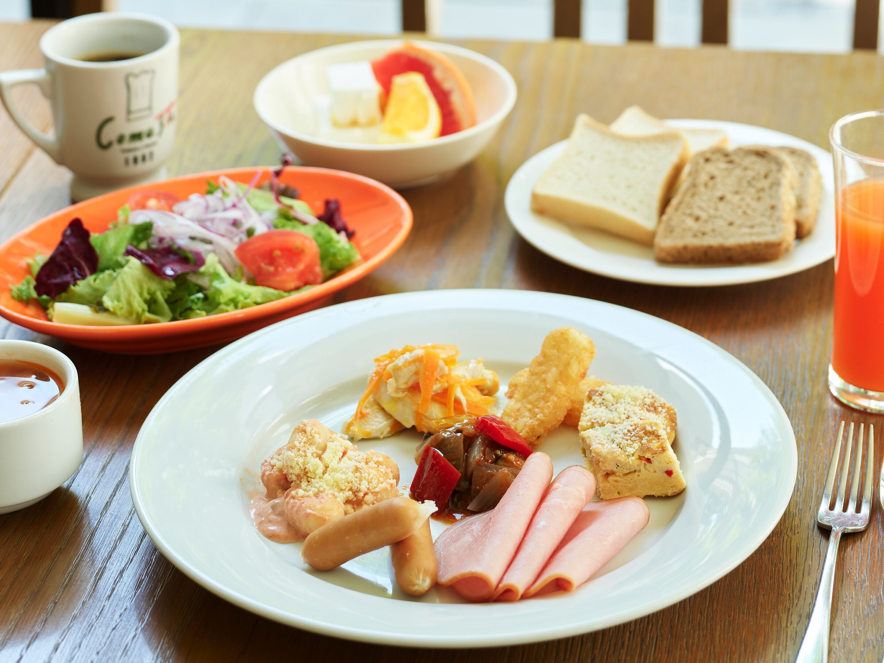 Une table avec une assiette de nourriture, un saladier de salade, une tasse de café et un verre de jus d’orange.