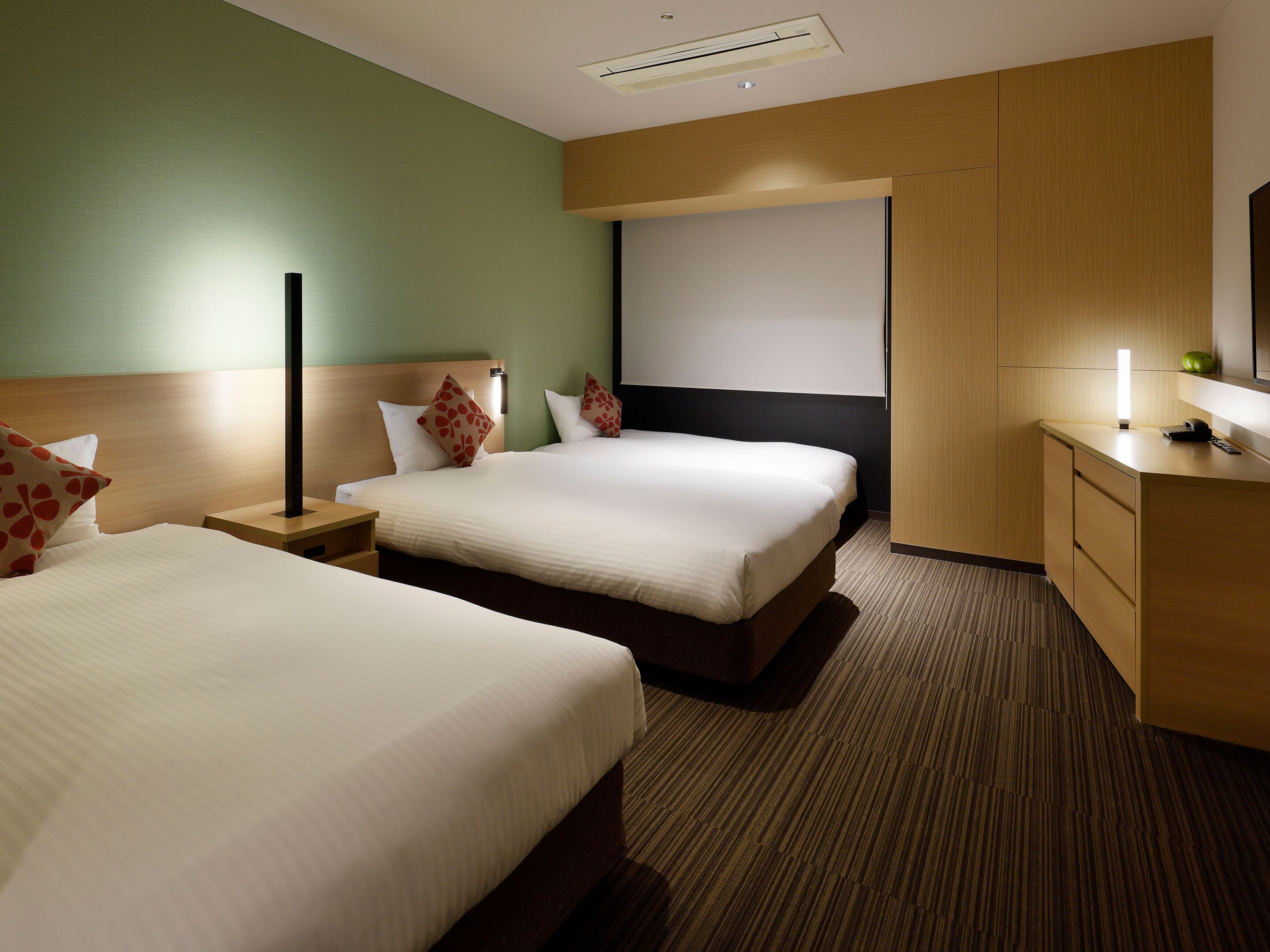 A hotel room with two beds, a desk, a mirror, and a wall-mounted TV.