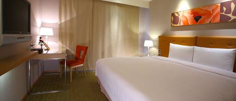 A hotel room with a bed, a desk, a chair, a TV, and a painting on the wall.
