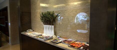 Un comptoir d’accueil avec des magazines, un téléphone et un vase avec des plantes.