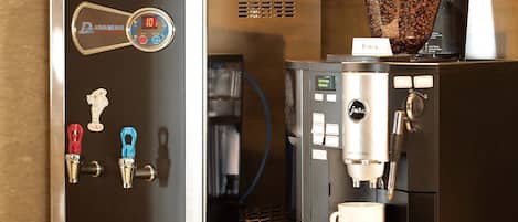 Una máquina de café con varios dispensadores y una jarra, una taza de café y un pequeño letrero en la encimera.